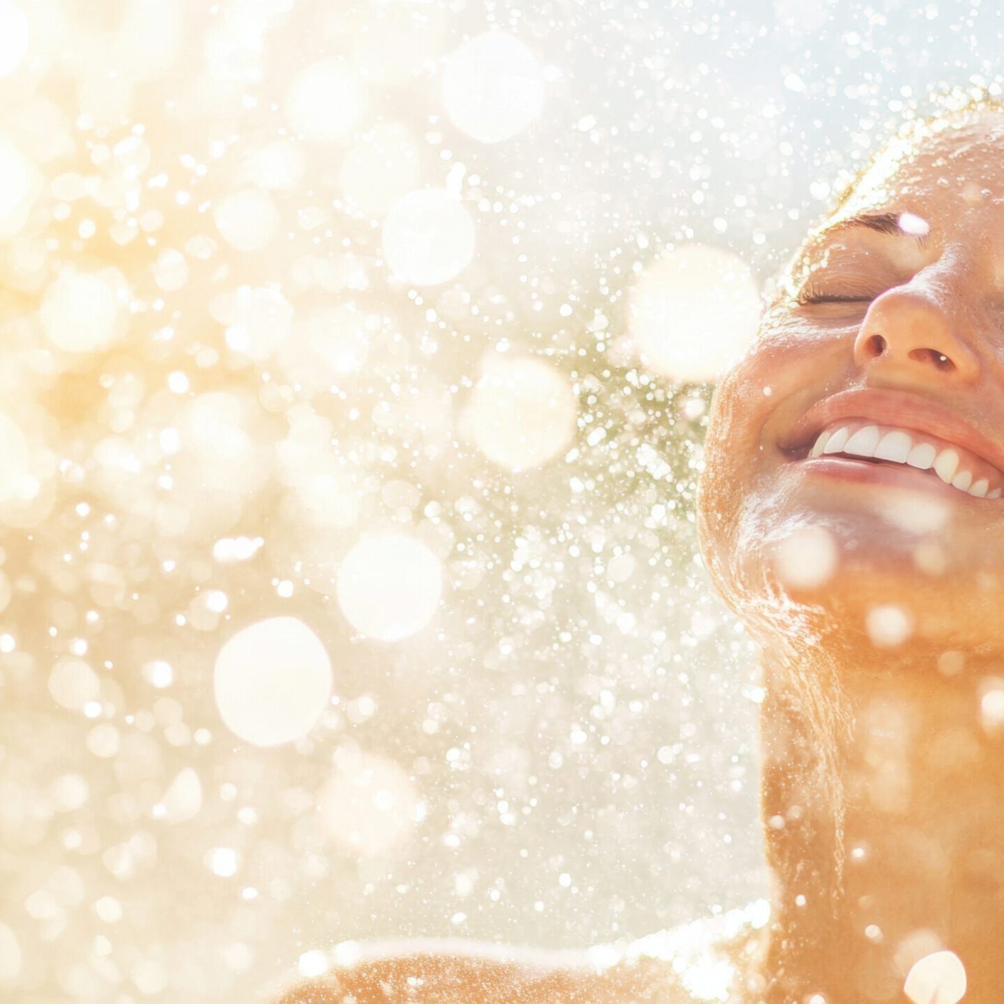 Enjoying a refreshing shower under the bright sunlight at a poolside A woman laughs joyfully while enjoying a refreshing shower under the sun, surrounded by sparkling water droplets.