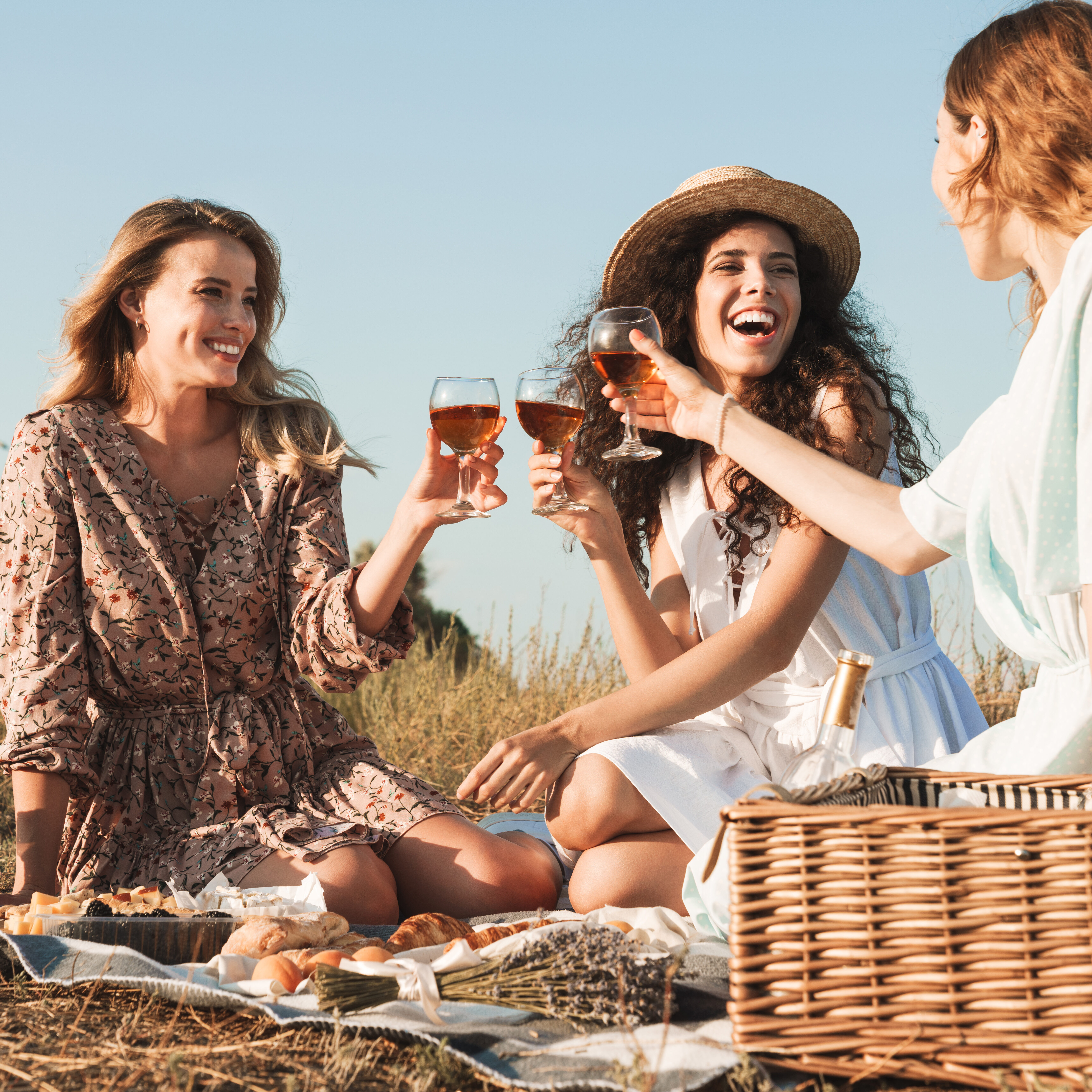 Photo of happy young three women drinking red wine while having picnic Photo of happy young women smiling and drinking red wine while having picnic at countryside during sunny day